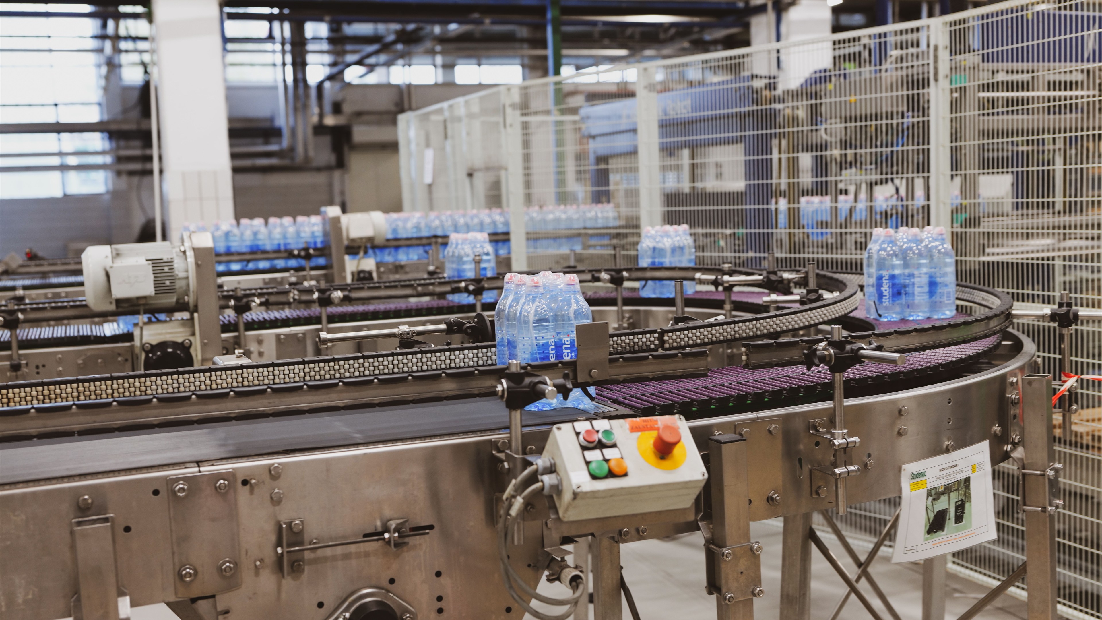 Línea de embotellado con transportadores curvos, botellas en movimiento y un tablero de control
